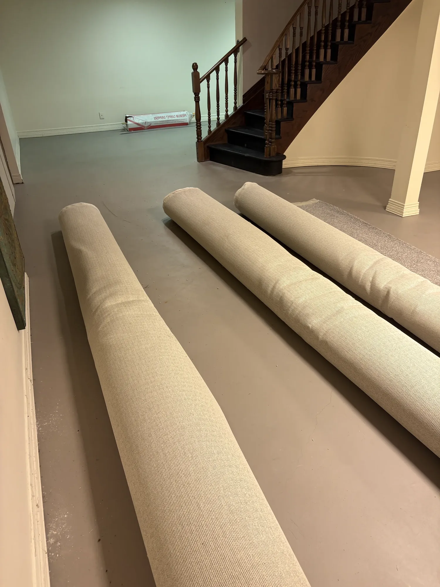 Rolls of carpet laid out on a painted concrete basement floor